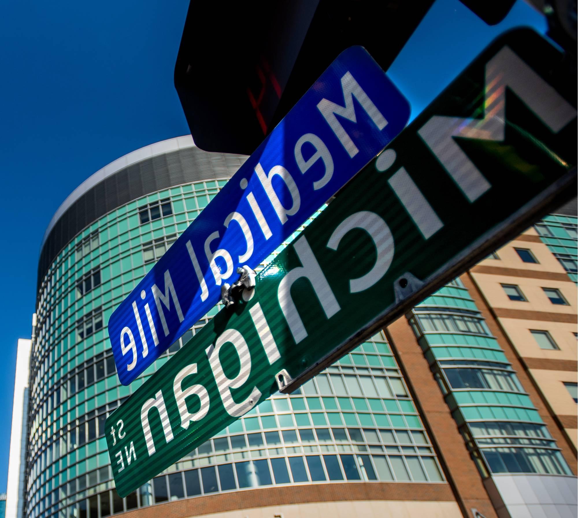 特写照片街道标志列出“密歇根街东北”和“医疗英里”, 远处有一座医疗大楼.